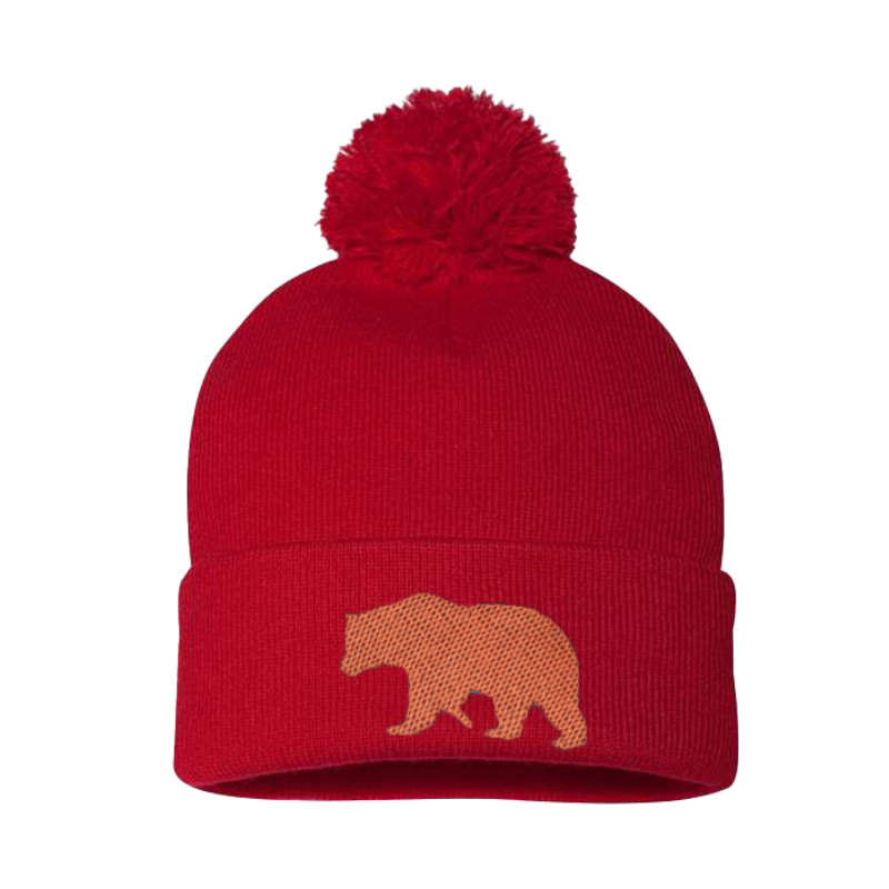 Red cuffed beanie with a Pom Pom. it has the silhouette of an embroidered copper bear