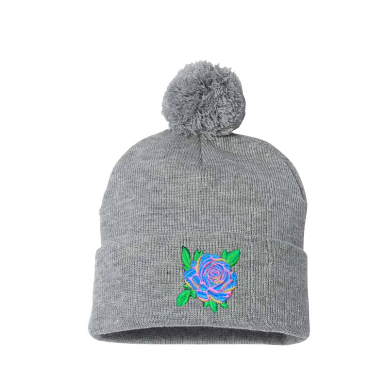 Light Gray cuffed beanie with a pom pom. It has a Blue Rose with pink, yellow and green leaves embroidered on the cuff