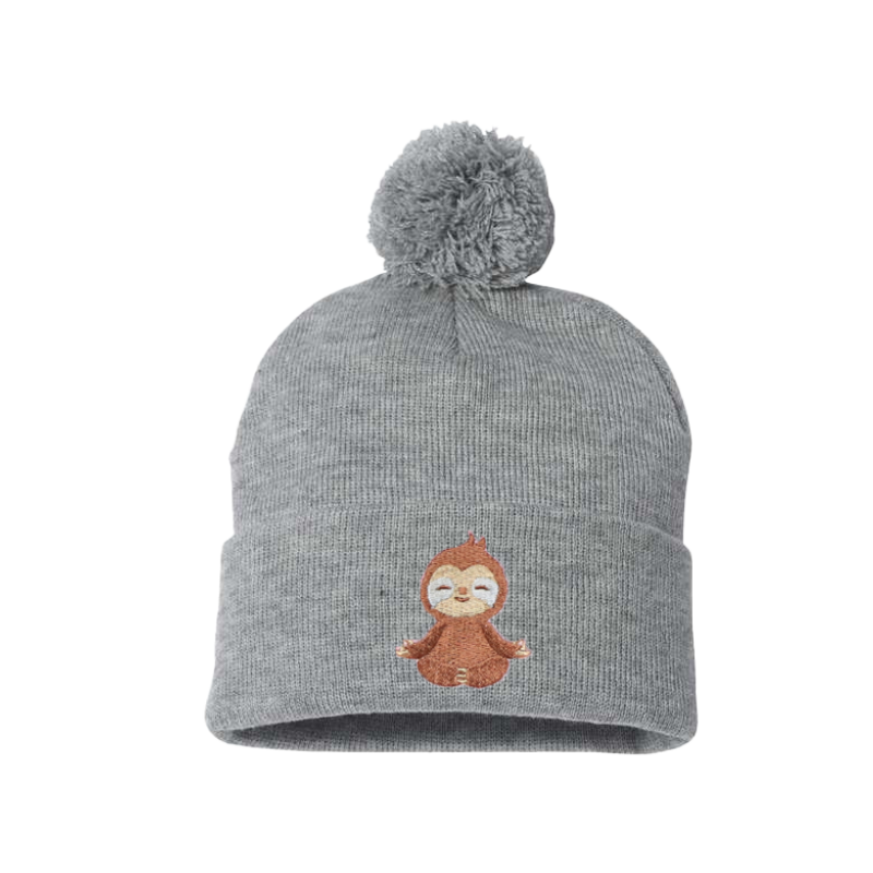 Light Gray cuffed beanie with a pom pom. This has an embroidery of a baby sloth meditating. The sloth is brown and creme placed on the cuff