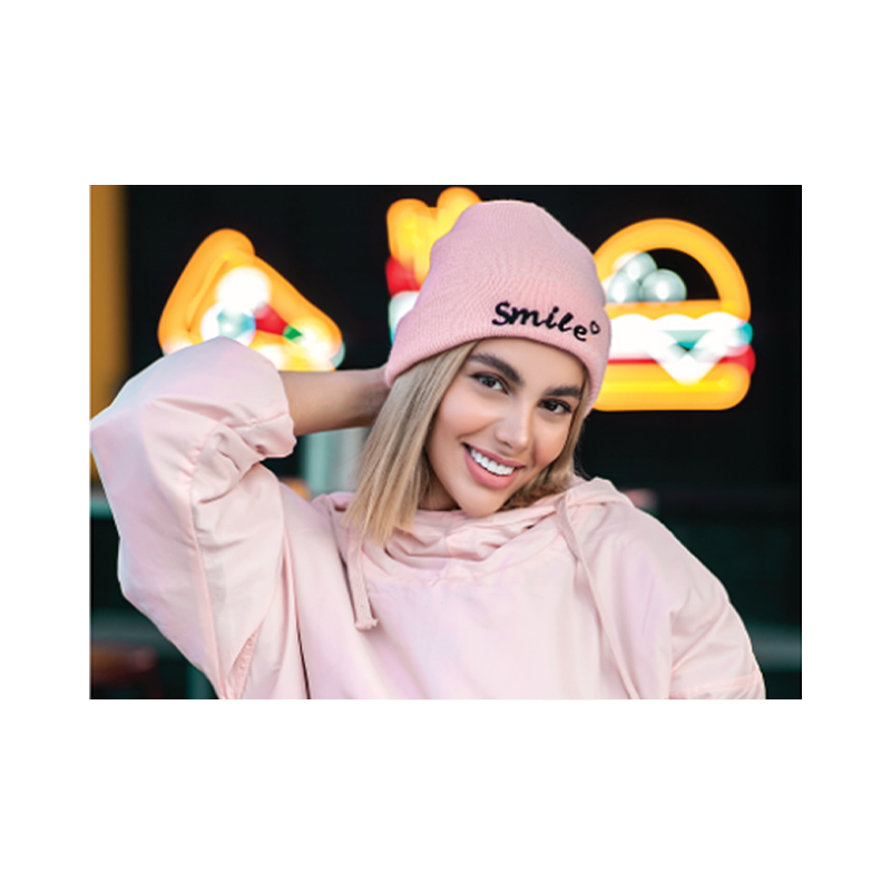 Young lady smiling and wearing a Pink Embroidered beanie. The Black embroidered in the cuff says the word Smile with a little heart on top of the last font E