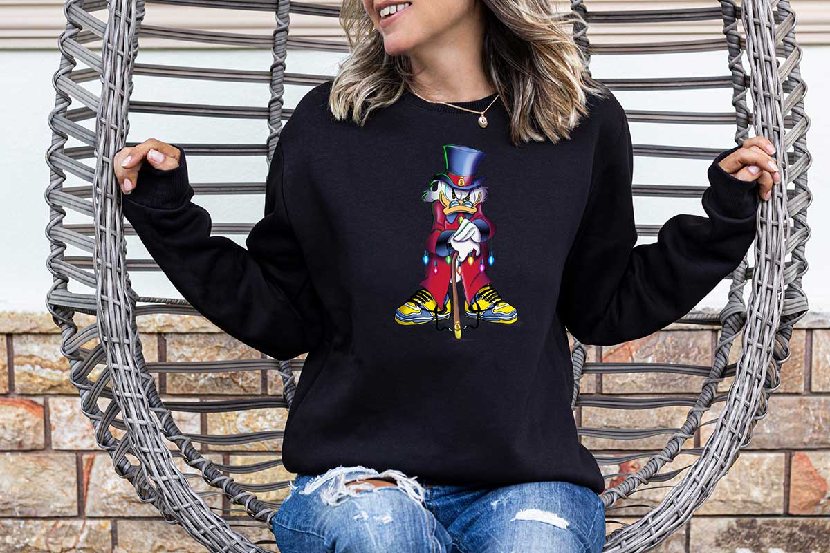 Woman wearing a black sweatshirt with a large screen printed of the scrooge McDuck. He is standing and angry leaning on his cane