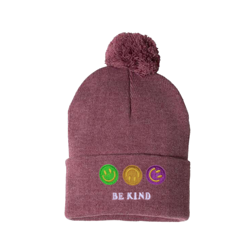 Heather cardinal cuffed beanie with a pom pom. It has an embroidery on the cuff  of three happy faces, green, gold and purple and a text in caps  Be kind