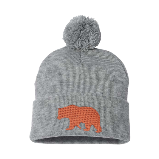 Light Gray cuffed beanie with a Pom Pom. it has the silhouette of an embroidered copper bear