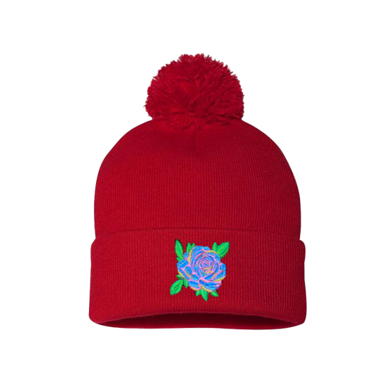 Red cuffed beanie with a pom pom. It has a Blue Rose with pink, yellow and green leaves  embroidered on the cuff 