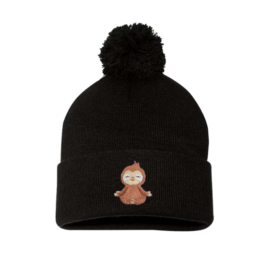 Black cuffed beanie with a pom pom. This has an embroidery of a baby sloth meditating. The sloth is brown and creme placed on the cuff 