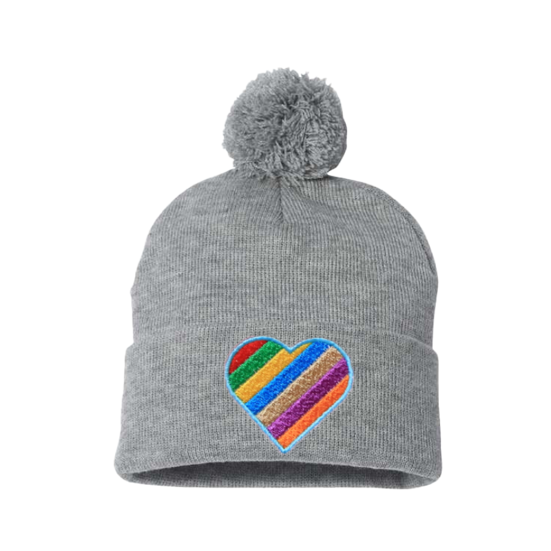 Light gray cuffed beanie with a pom pom. It has a heart embroidered with the Pride colors on the cuff