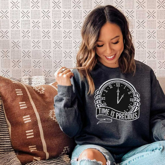 Woman wearing a dark heather sweatshirt with a large screen printed of a big white clock and a text underneath time is precious