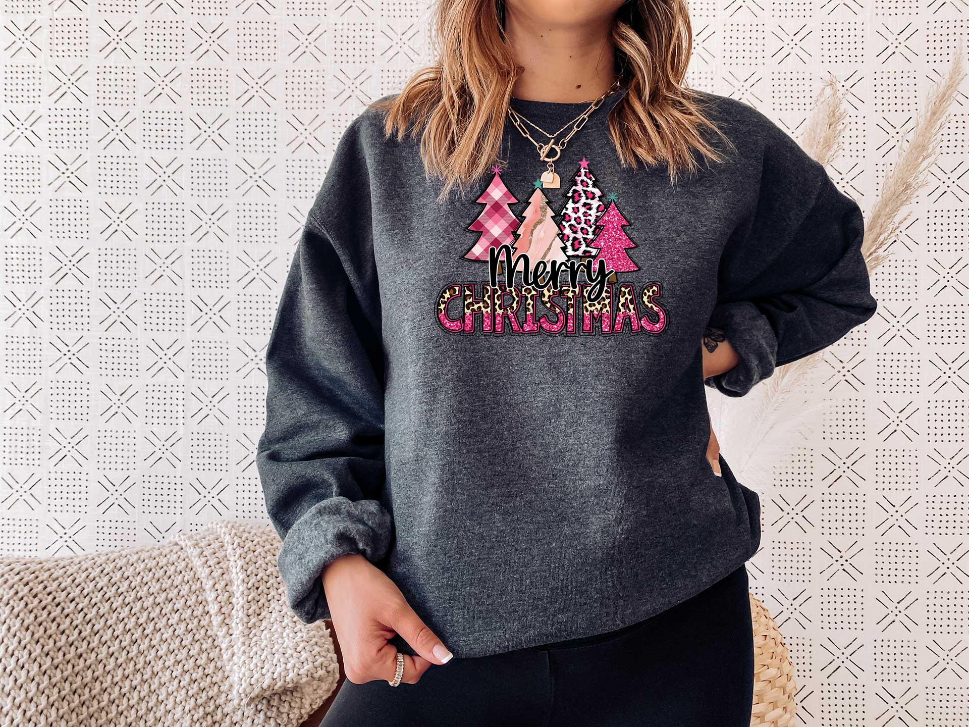 Young lady wearing a dark heather sweater with a big screen printed on the front. This one has four different pink Christmas trees and a text in black Merry and Christmas in pink and cheetah colors