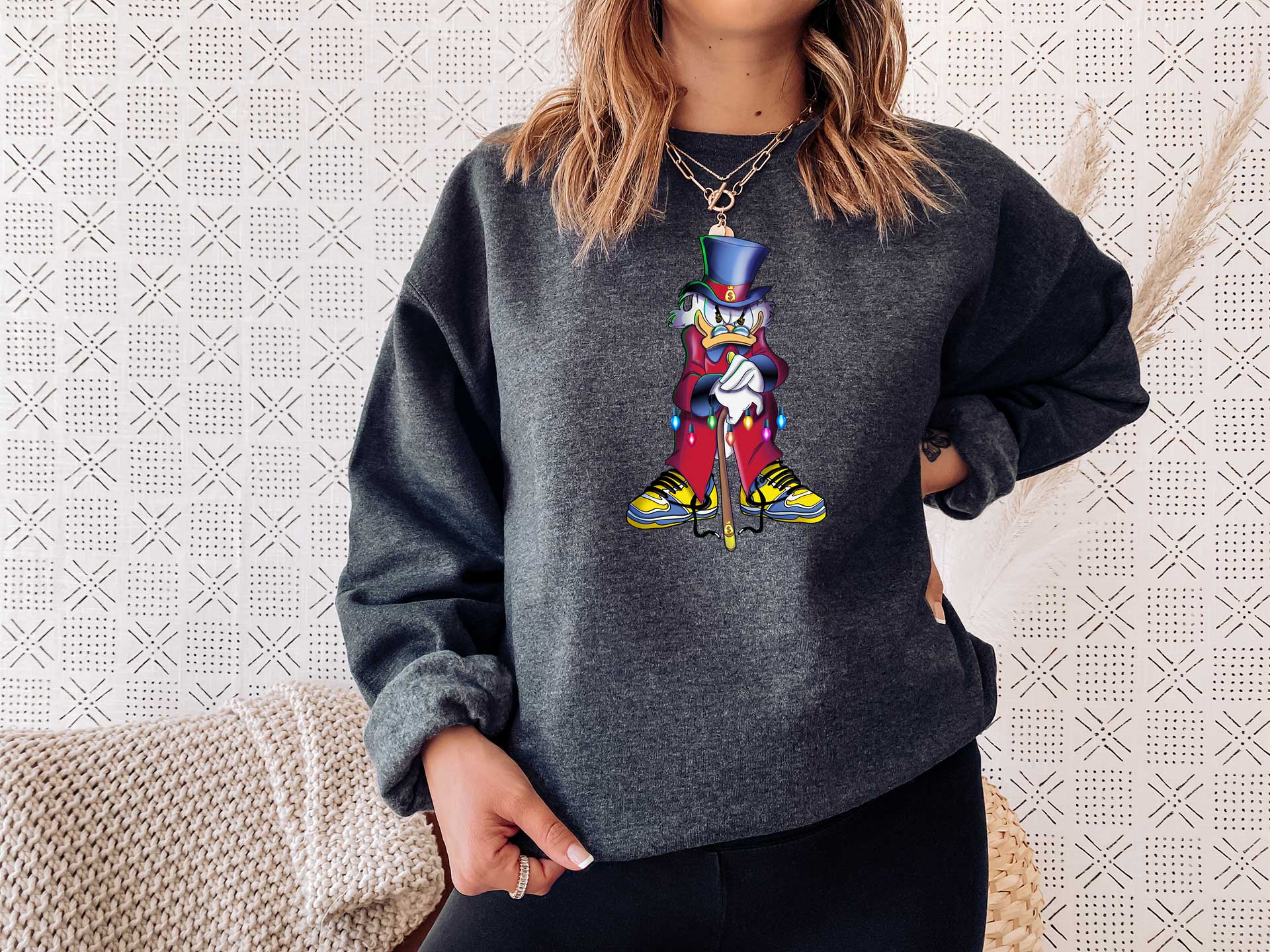 Woman wearing a dark heather sweatshirt with a large screen printed of the scrooge McDuck. He is standing and angry leaning on his cane